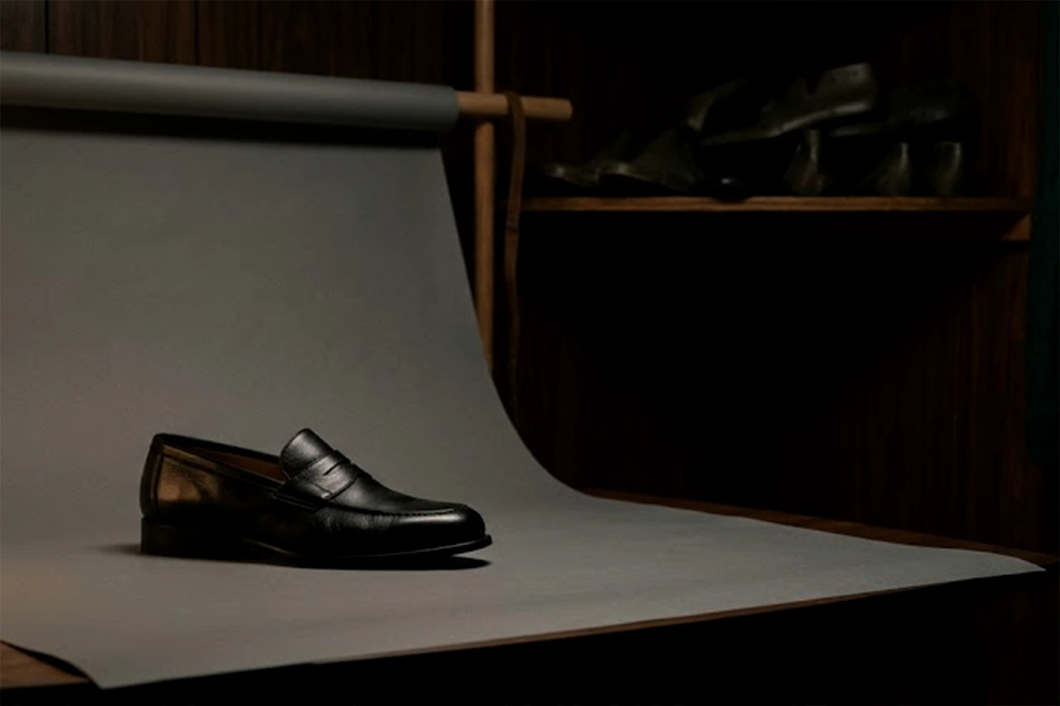 A single black loafer on a sweep of grey paper, lit from the left by one paper lamp