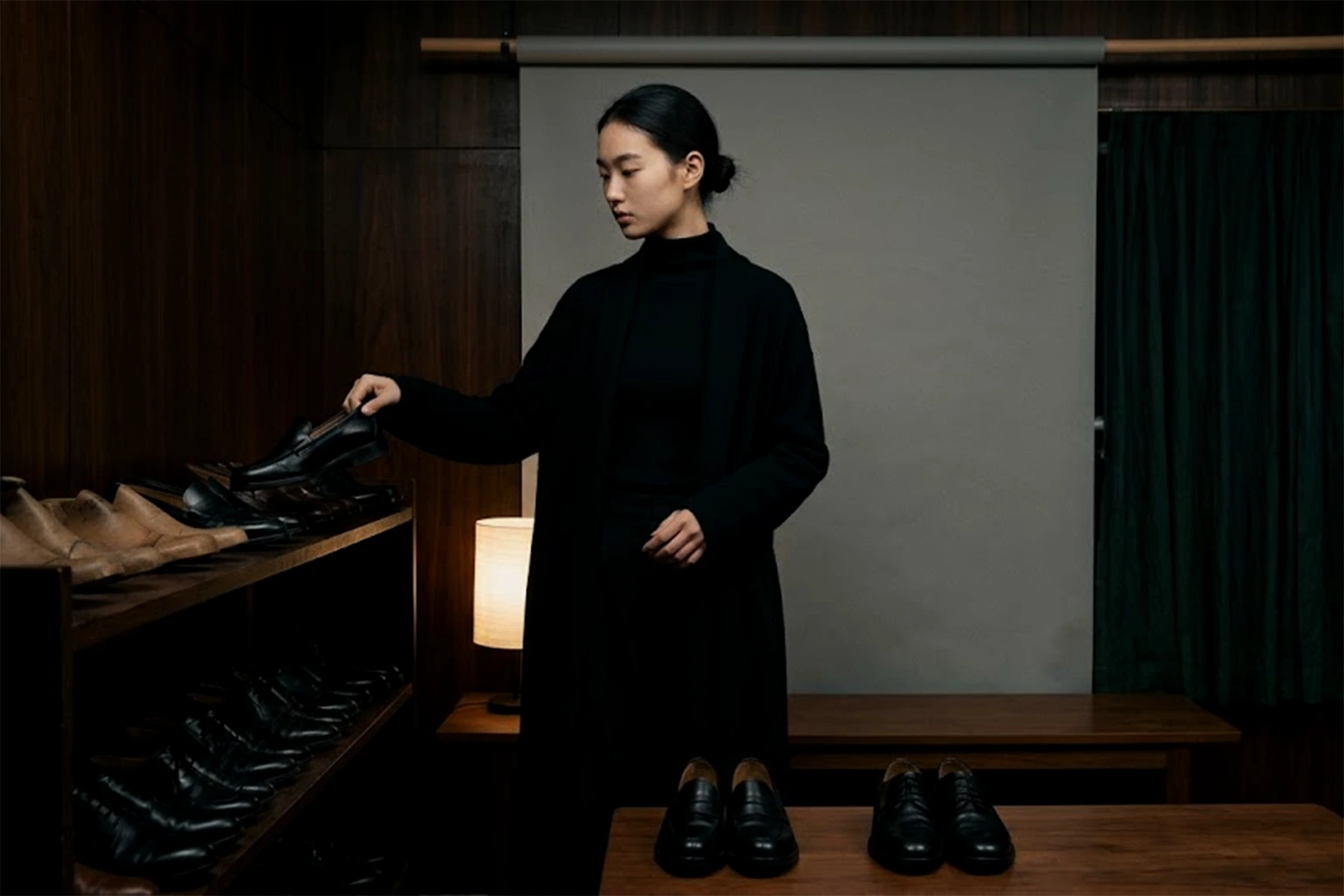 A person taking one shoe from a shelf, with two chosen pairs of loafers set out on the table